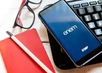 Smartphone com aplicativo oficial do ENEM sobre teclado e caderno vermelho.