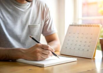 Pessoa anotando em caderno ao lado de calendário de mesa consultando datas de maio de 2026