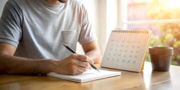 Pessoa anotando em caderno ao lado de calendário de mesa consultando datas de maio de 2026