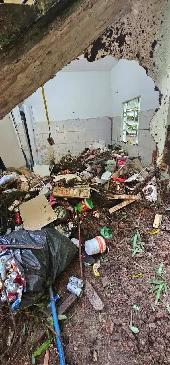 Danos em residência após enchente em Juiz de Fora e Ubá Sala destruída por enchente, com entulho, lama e objetos danificados, ilustrando os danos causados por eventos extremos.