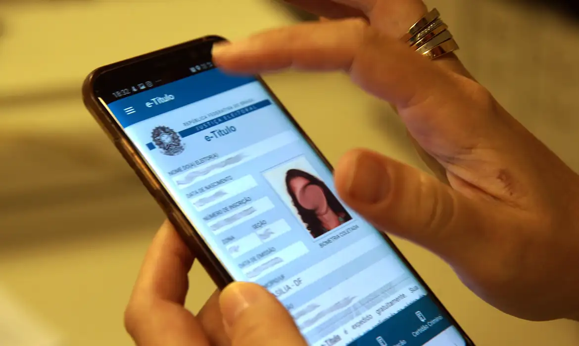 Como consultar a situação eleitoral pelo celular usando o aplicativo e-Título em 2026 Pessoa consultando o aplicativo e-Título no celular para verificar a situação eleitoral antes do prazo final de regularização