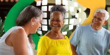Três pessoas idosas sorrindo sentadas, fundo com elementos gráficos verde e amarelo, simbolizando o pagamento do 13º salário do INSS.