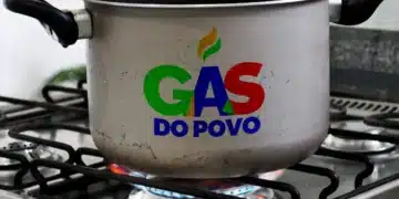 Panela de alumínio com alças pretas sobre boca de fogão acesa, exibindo logomarca "Gás do Povo" em cores verde, azul e vermelho