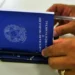 Mãos de pessoa segurando Carteira de Trabalho e Previdência Social azul sobre mesa branca com caneta ao lado, representando os direitos trabalhistas ampliados pela nova lei de licença-paternidade sancionada em 31 de março de 2026, que garante estabilidade no emprego, salário-paternidade pelo INSS e afastamento de até 20 dias para trabalhadores com carteira assinada, MEIs, domésticos, avulsos e segurados especiais