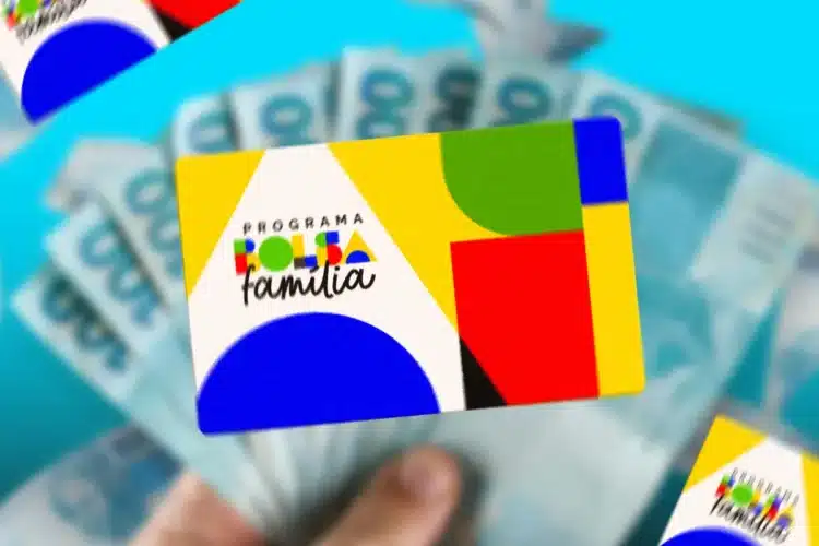 Bolsa Família 2026 Cartão colorido do Programa Bolsa Família segurado por mão com cédulas de real desfocadas ao fundo.