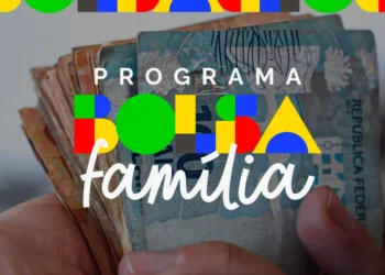Mãos segurando notas de real com a logomarca do Programa Bolsa Família — pagamentos de abril iniciam no dia 16