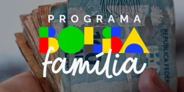 Mãos segurando notas de real com a logomarca do Programa Bolsa Família — pagamentos de abril iniciam no dia 16