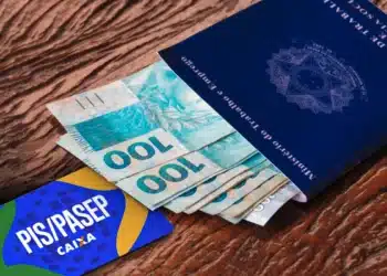 Carteira de trabalho azul do Ministério do Trabalho sobre notas de R$ 100 ao lado de cartão PIS/Pasep da Caixa.