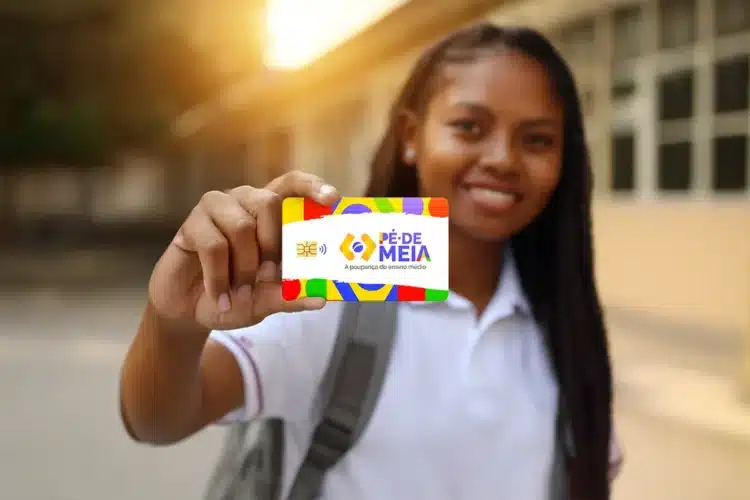 Pagamento Pé-de-Meia 2026 Jovem estudante negra sorri e segura o cartão do programa Pé-de-Meia, da poupança do ensino médio, em frente a uma escola.