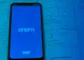 Smartphone exibindo logo do Enem e INEP em tela azul sobre páginas de livro de matemática com equações exponenciais.