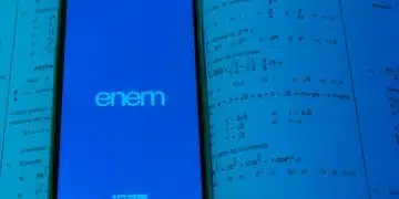 Smartphone exibindo logo do Enem e INEP em tela azul sobre páginas de livro de matemática com equações exponenciais.