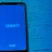 Smartphone exibindo logo do Enem e INEP em tela azul sobre páginas de livro de matemática com equações exponenciais.