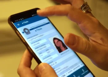 Pessoa consulta o aplicativo e-Título no celular, para verificar a situação eleitoral e realizar a regularização do título pelo portal do TSE.