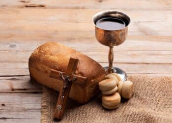 Pão rústico, cálice de vinho prateado e um crucifixo de madeira sobre uma mesa rústica. Elementos que simbolizam a Sexta-Feira Santa e o período de feriado religioso.