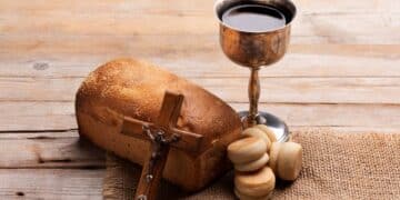 Pão rústico, cálice de vinho prateado e um crucifixo de madeira sobre uma mesa rústica. Elementos que simbolizam a Sexta-Feira Santa e o período de feriado religioso.