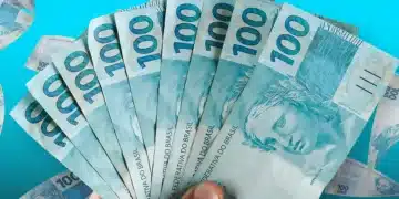 Mão segurando leque de notas de R$ 100 com outras cédulas ao fundo — valores esquecidos nos bancos aguardam resgate em 2026