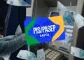 Cartão PIS/Pasep da Caixa, azul, com notas de 100 reais ao redor e caixa eletrônico ao fundo