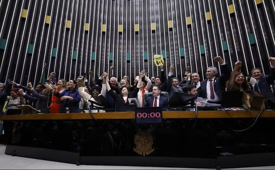 Deputados comemoram aprovação do fim da escala 6x1 no plenário da Câmara com braços erguidos e cartaz amarelo