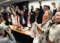 Parlamentares de mãos dadas levantadas celebram aprovação da PEC contra escala 6x1, com camisetas e cartazes da campanha