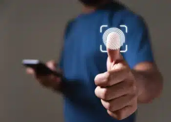 Pessoa de camiseta azul toca ícone de impressão digital em tela virtual, segurando smartphone na outra mão.