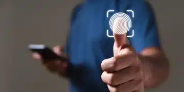 Pessoa de camiseta azul toca ícone de impressão digital em tela virtual, segurando smartphone na outra mão.