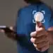 Pessoa de camiseta azul toca ícone de impressão digital em tela virtual, segurando smartphone na outra mão.