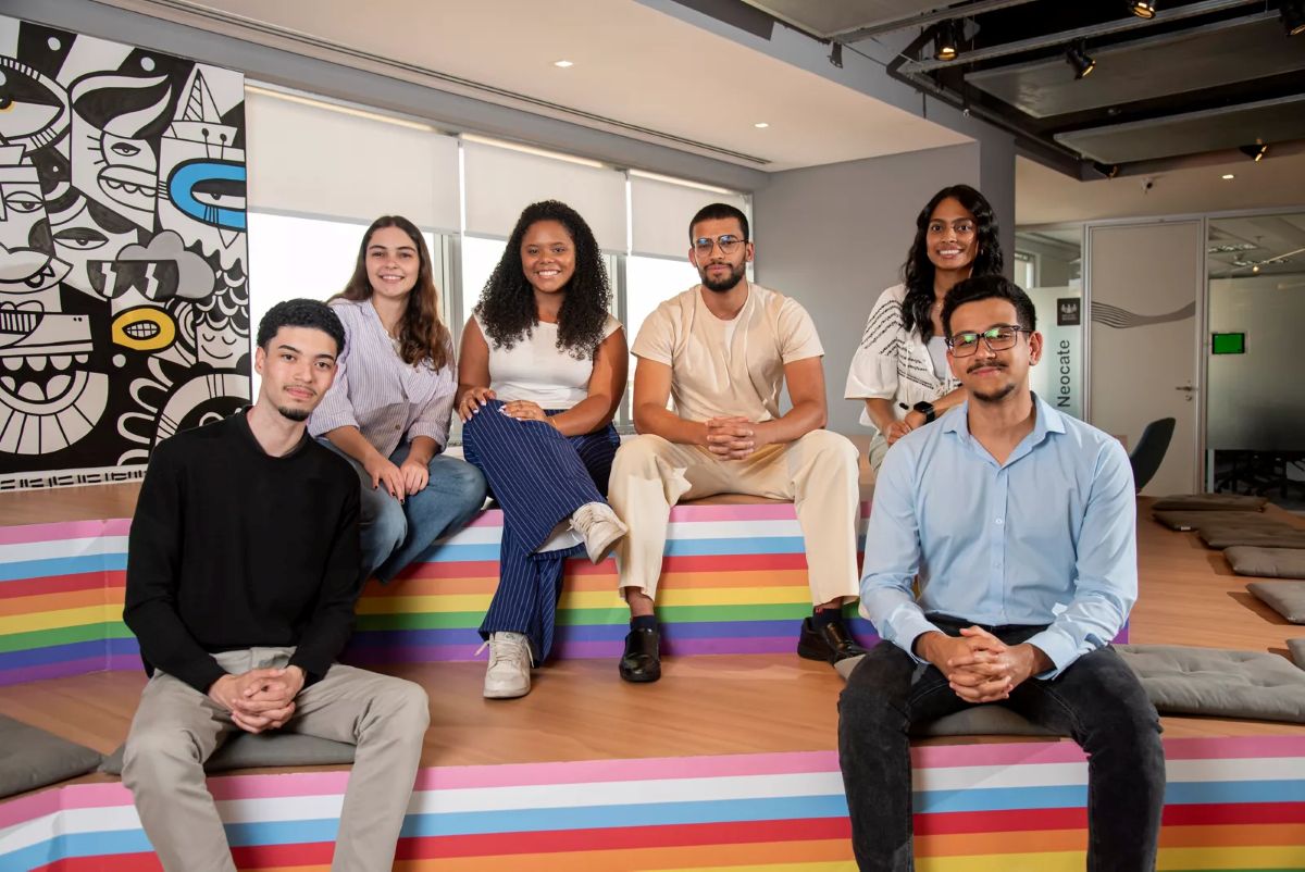 Seis jovens sorriem sentados em um banco listrado