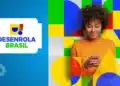 Mulher negra de blusa laranja usando celular com logo do Desenrola Brasil ao lado em fundo colorido.