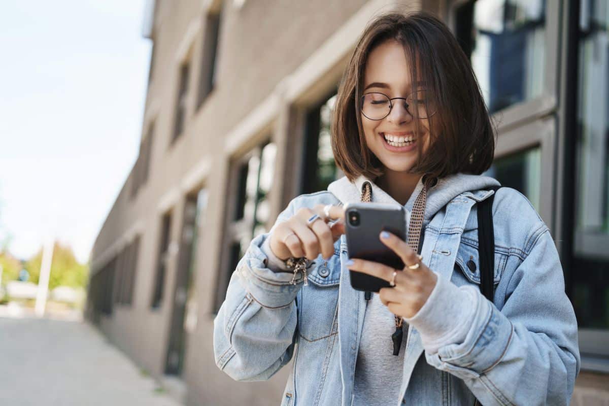 Estudante sorrindo utiliza o celular na rua