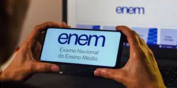 Pessoa segurando celular com página do Enem aberta em frente a notebook