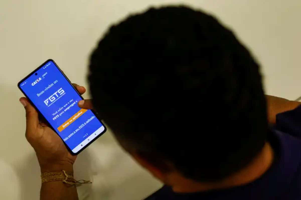 Homem visto de costas segura um celular com o aplicativo do FGTS na tela