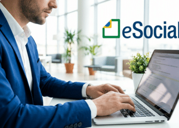 Empresário digitando em laptop com logo do eSocial em ambiente corporativo.