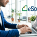 Empresário digitando em laptop com logo do eSocial em ambiente corporativo.