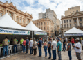 Fila de pessoas aguardando atendimento em tendas brancas com faixas do Governo do Brasil na Rua na Praça da Alfândega