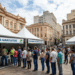 Fila de pessoas aguardando atendimento em tendas brancas com faixas do Governo do Brasil na Rua na Praça da Alfândega