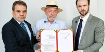 Três homens de terno e chapéu seguram decreto assinado, fita verde-amarela na capa
