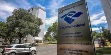 Placa da Receita Federal em frente a prédio, céu azul e carros estacionados