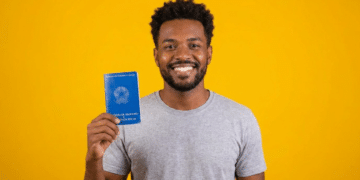 Jovem segura carteira de trabalho brasileira sorrindo com fundo amarelo.