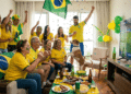 Grupo de 10 pessoas com camisas amarelas da seleção e pinturas faciais celebra gol assistindo TV com placar Brasil 2x0 Argentina