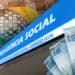 Fachada do edifício-sede da Previdência Social do INSS ao lado de cédulas de cem reais, representando os pagamentos acima do salário mínimo em julho de 2026.