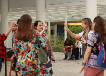 Cinco pessoas trocam sinais em Libras em área aberta, mochilas e roupas coloridas