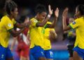 Jogadoras da seleção brasileira de futebol feminino, de uniforme amarelo e azul, comemoram juntas em campo, referência à Copa do Mundo Feminina citada no projeto