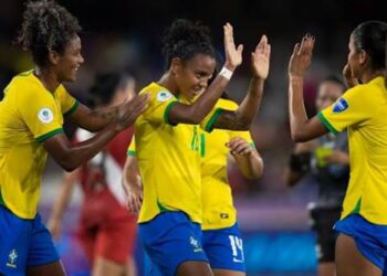 Jogadoras da seleção brasileira de futebol feminino, de uniforme amarelo e azul, comemoram juntas em campo, referência à Copa do Mundo Feminina citada no projeto