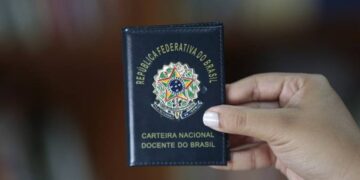 Imagem ilustrativa de mão segurando a Carteira Nacional Docente do Brasil, documento de capa azul com o brasão da República