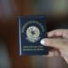 Imagem ilustrativa de mão segurando a Carteira Nacional Docente do Brasil, documento de capa azul com o brasão da República