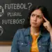 Jovem mulher faz expressão confusa em frente a quadro negro com pergunta sobre plural de futebol e desenhos de bolas