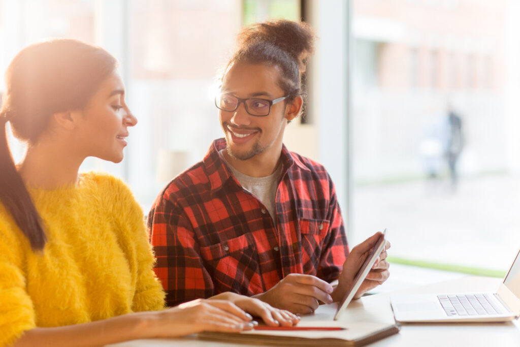 Leitura dos conceitos atribuídos a cursos e faculdades Imagem ilustrativa de dois estudantes consultando informações em um tablet sobre a mesa, cena ligada à análise das notas atribuídas a cursos superiores.