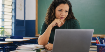 Professora utiliza notebook em sala de aula durante formação sobre inteligência artificial para educadores.