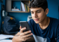 Estudante brasileiro usando smartphone durante preparação para o Enem em ambiente de estudos.
