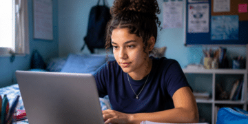 Estudante se preparando para o Enem 2026 com notebook e materiais de estudo em ambiente residencial.